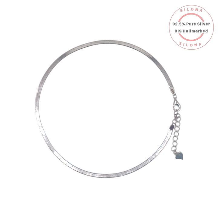 Silona Classic Herringbone Silver Anklet, a flat snake chain design in pure 92.5 silver, laid in a circle on a white background with an adjustable clasp and heart charm.