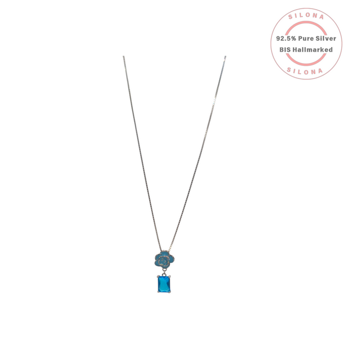 A silver box chain necklace featuring a blue enamel rose pendant with a dangling rectangular aqua blue gemstone, on a white background.