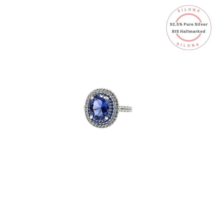 A royal blue tanzanite-hue cubic zirconia ring with a double halo of blue and clear stones, crafted in 92.5 sterling silver, shown on a white background.