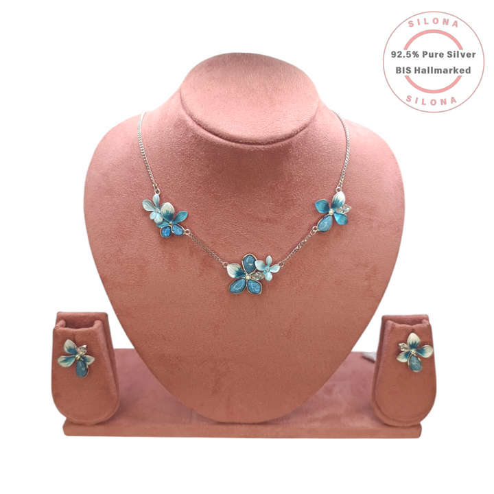 Silona's Azure Bloom floral necklace and earring set, featuring blue and white enamel flowers on pure 92.5 silver, displayed on a pink bust.