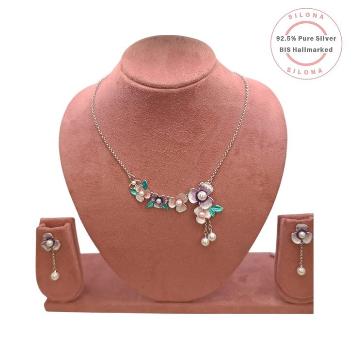 Silona's Enamel Bloom Floral Necklace and Earring Set in 92.5 silver, featuring pastel pink and purple flowers with pearl centres and mint green leaves, displayed on a pink bust.