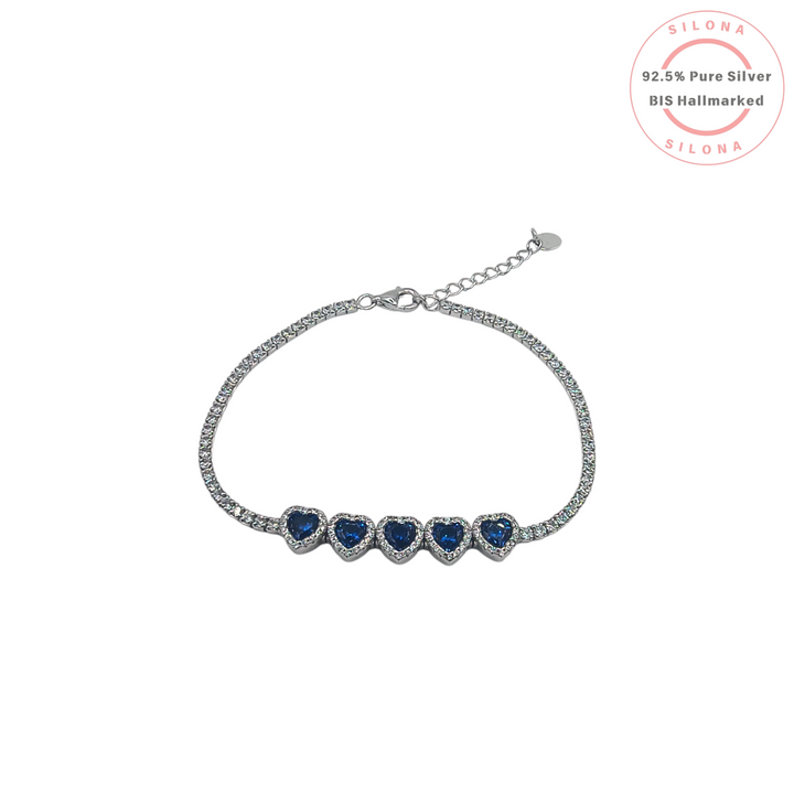 Silona's Oceanic Heart Tennis Bracelet in 92.5 silver, featuring five sapphire-blue heart stones with a halo of cubic zirconia on a sparkling band.