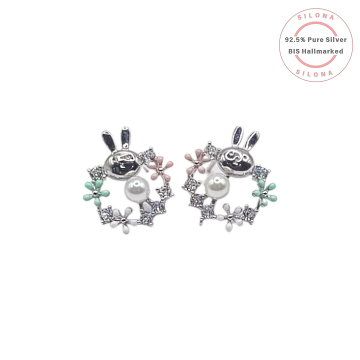 A pair of sterling silver stud earrings shaped like a bunny inside a floral wreath, detailed with pastel pink and green enamel, a pearl, and cubic zirconia stones.