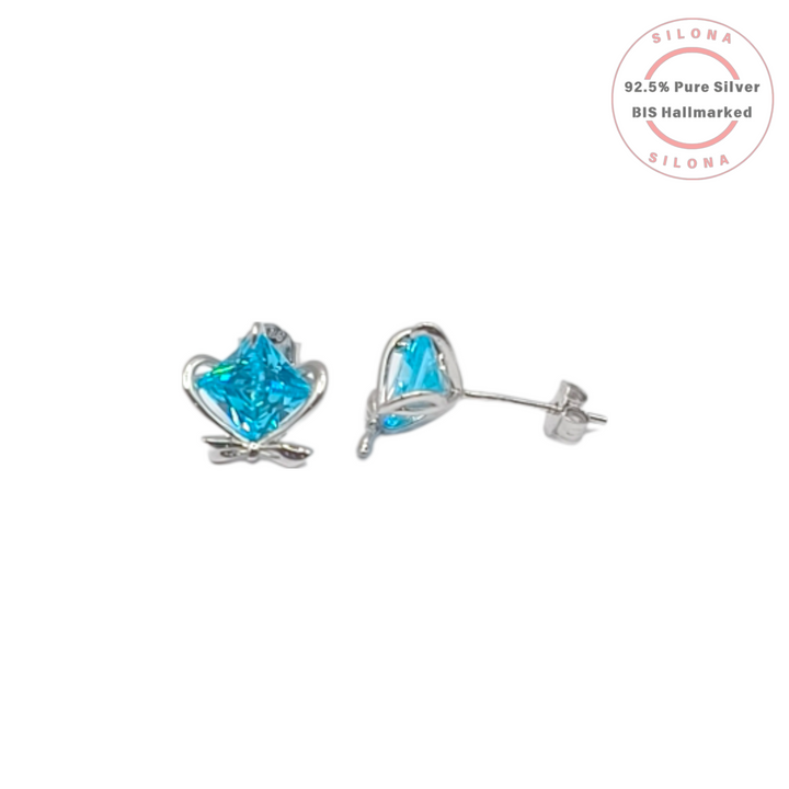 A pair of sterling silver stud earrings featuring a princess-cut, aqua blue cubic zirconia stone set within a delicate heart and bow design, on a white background.