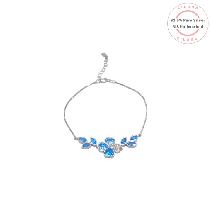 Delicate silver bracelet featuring a central clover flower made of four heart-shaped Swiss blue stones, with a pavé accent and blue leaf details on a box chain.