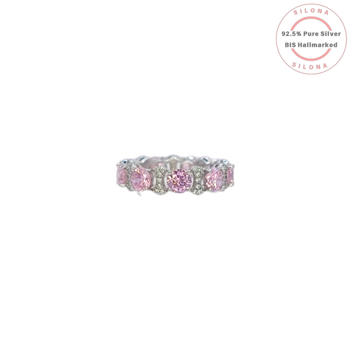 A silver eternity ring featuring large, round, blush pink cubic zirconia stones, interspersed with clusters of small clear pavé stones, on a white background.