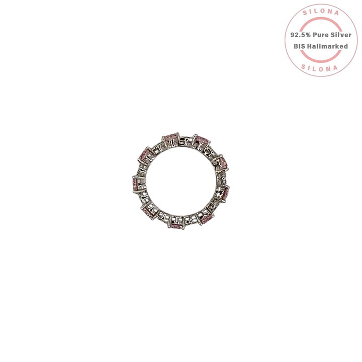 A silver eternity ring featuring large, round, blush pink cubic zirconia stones, interspersed with clusters of small clear pavé stones, on a white background.