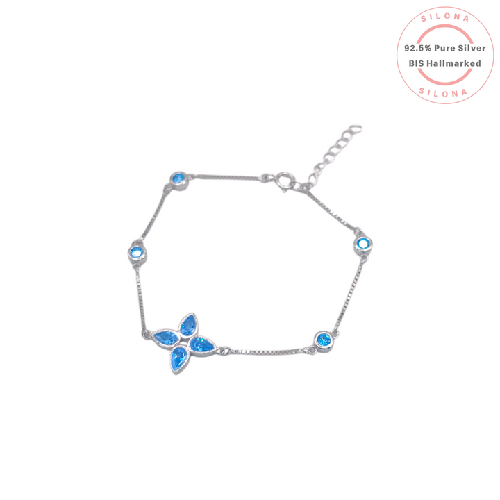An elegant silver bracelet featuring a central four-leaf clover motif made from pear-shaped aqua blue stones, with smaller round blue stones set along a delicate box chain.