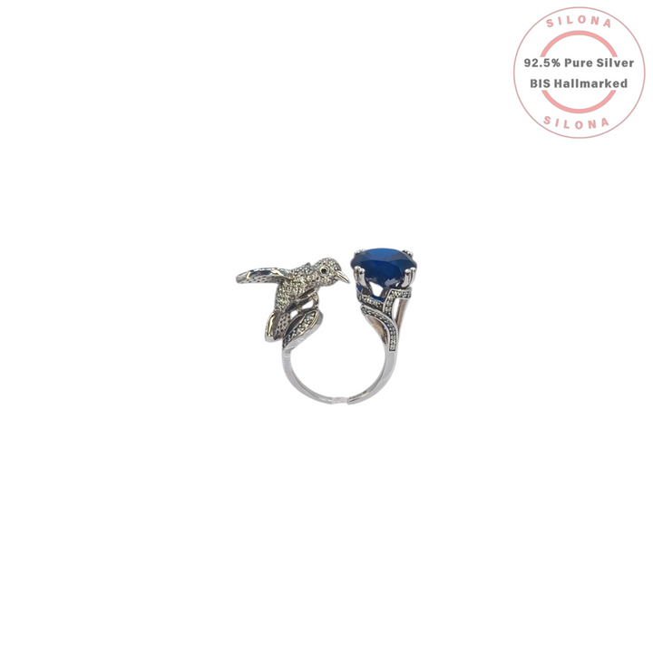 Silona Sculptural Hummingbird Ring in 92.5 silver, featuring a pavé set bird and a large, deep blue faceted stone, on a white background.