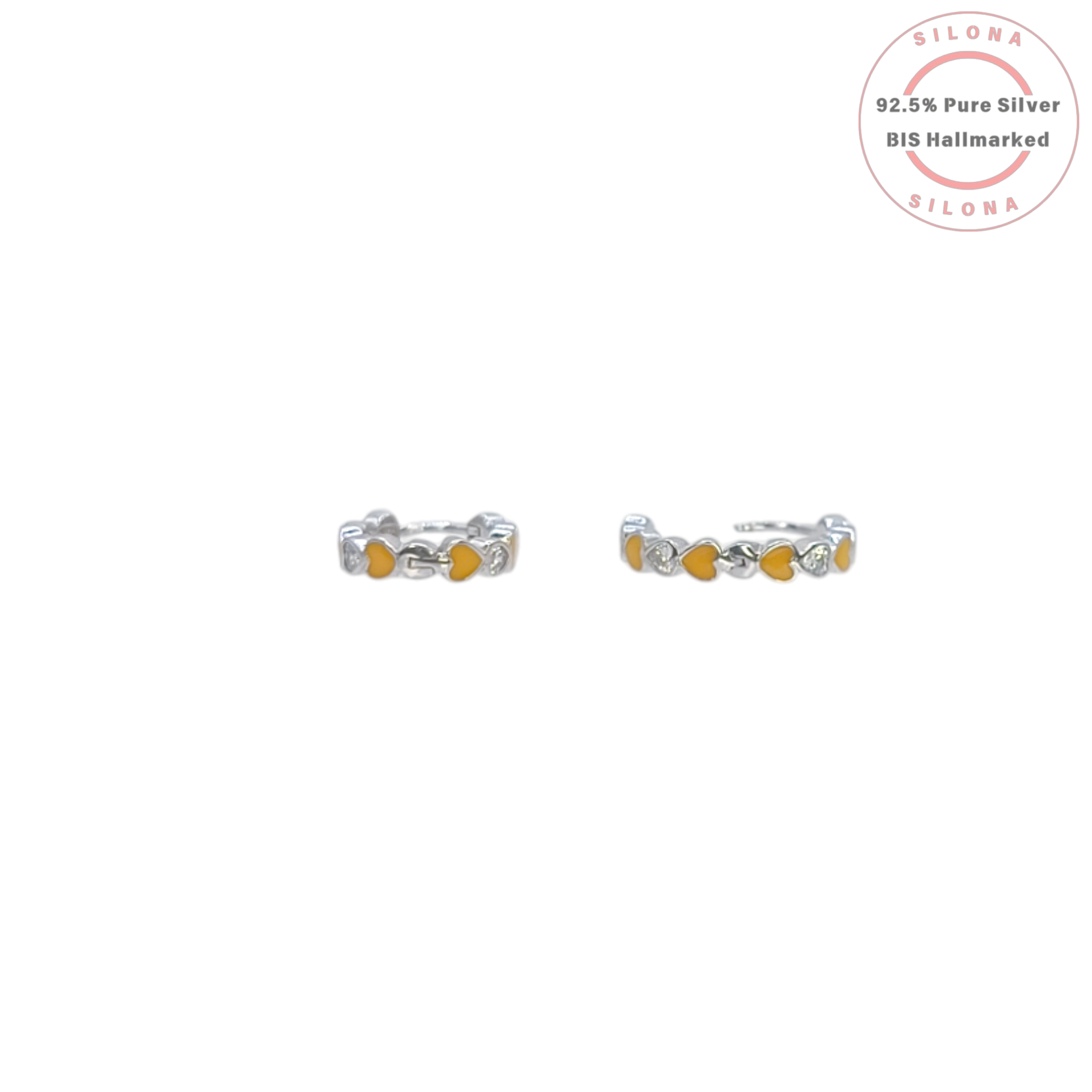 A pair of silver huggie hoop earrings with a repeating pattern of hearts, featuring yellow, mustard, and peach enamel, and a single clear cubic zirconia heart, on a white background.