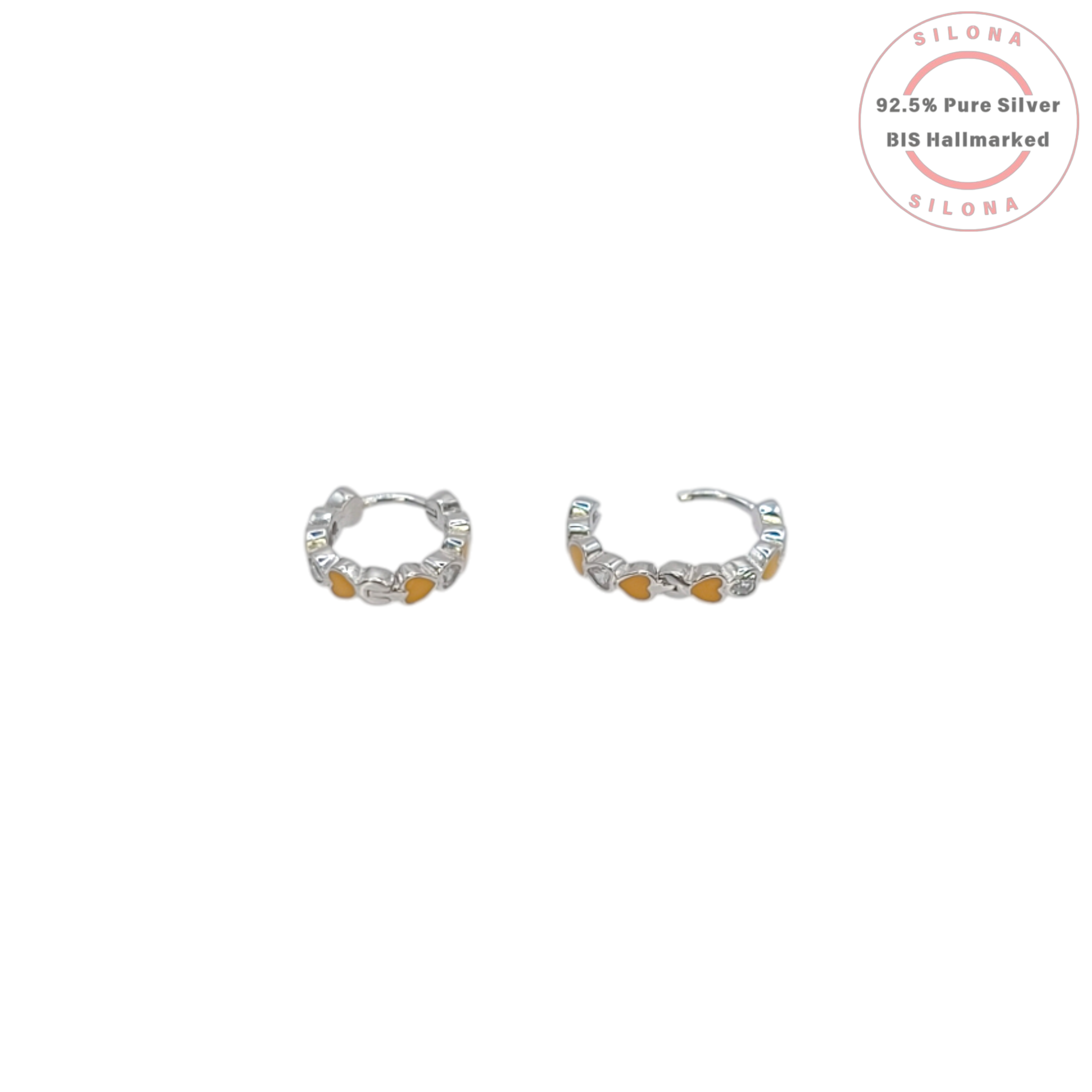 A pair of silver huggie hoop earrings with a repeating pattern of hearts, featuring yellow, mustard, and peach enamel, and a single clear cubic zirconia heart, on a white background.