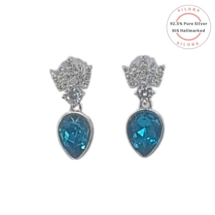 A pair of elegant silver drop earrings featuring a pavé cubic zirconia top stud and a large, pear-shaped blue crystal drop on a white background.