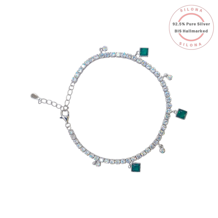 A Silona silver tennis bracelet with clear cubic zirconia stones, featuring dangling charms of square-cut emerald green stones and round clear stones, on a white background.
