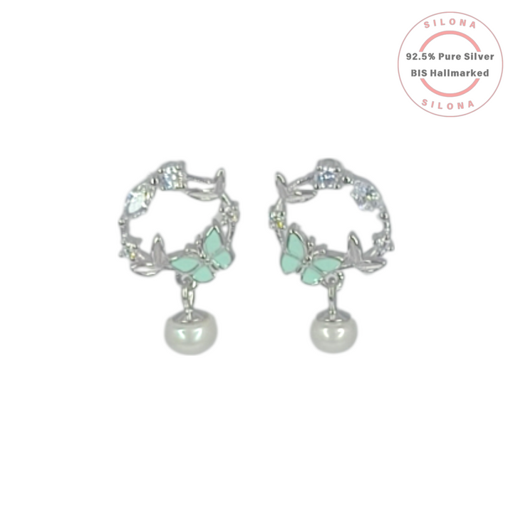Silona's silver hoop earrings featuring a mint-green enamel butterfly motif, sparkling cubic zirconia, and a dangling white pearl drop on a white background.
