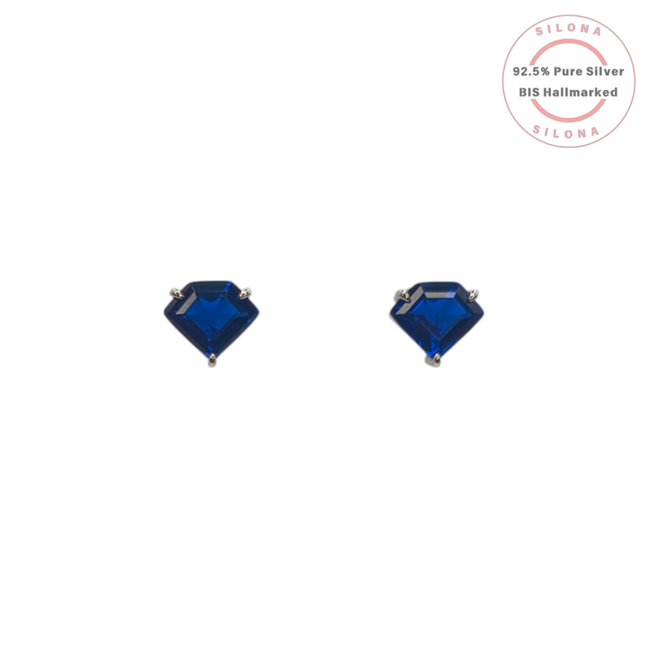 A pair of minimalist kite-cut stud earrings with deep sapphire-blue stones, set in 92.5 sterling silver, on a white background.