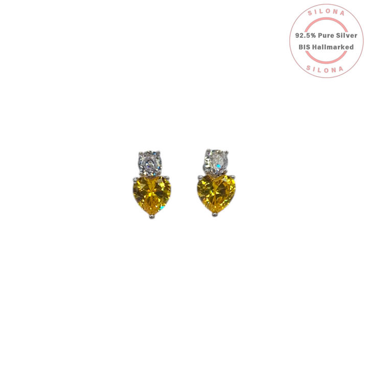 A pair of Silona silver stud earrings, each featuring a heart-shaped canary yellow cubic zirconia stone below a small, round, clear cubic zirconia stone, on a white background.