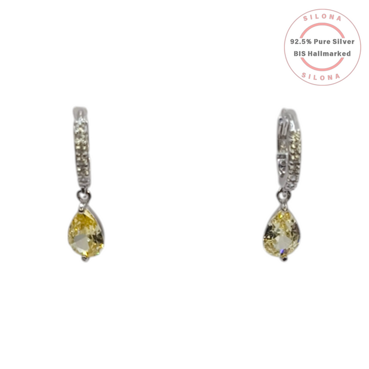 A pair of Silona silver huggie earrings with pavé set cubic zirconia and a dangling pear-cut canary yellow stone on a white background.