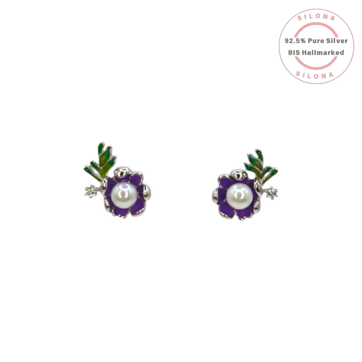 A pair of silver stud earrings shaped like purple enamel flowers with a central pearl, green enamel leaves, and a small cubic zirconia accent, on a white background.