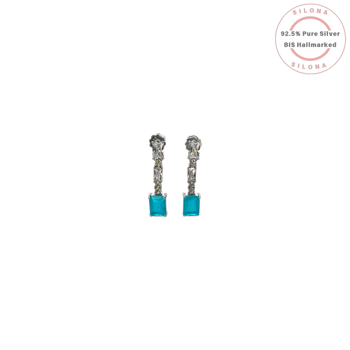A pair of modern silver drop earrings with clear baguette-cut stones and a large rectangular aqua blue cubic zirconia stone at the drop, on a white background.