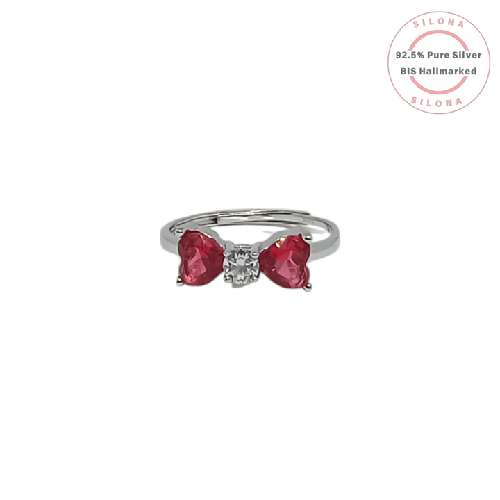 Silona's Chic Ruby-Hued Heart Bow Ring in pure 92.5 silver, featuring two red heart stones and a central solitaire on an adjustable band.