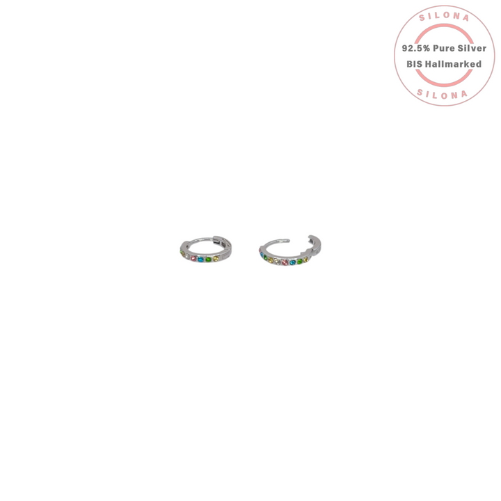 A pair of Silona's rainbow confetti huggie hoop earrings in pure 92.5 silver with multicolored stones, on a white background.