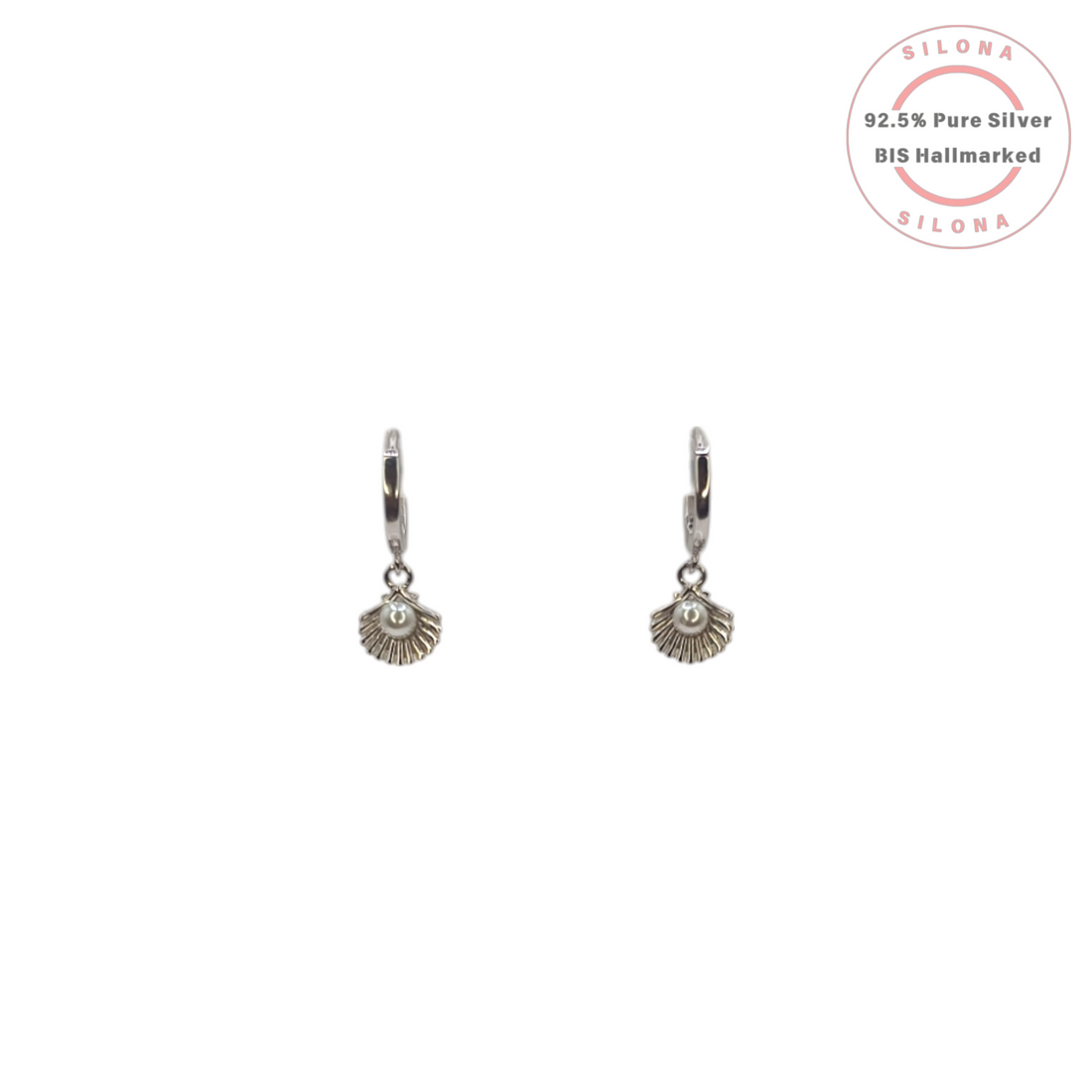 A pair of Silona silver huggie hoop earrings with a dangling seashell charm cradling a small white pearl, on a white background.
