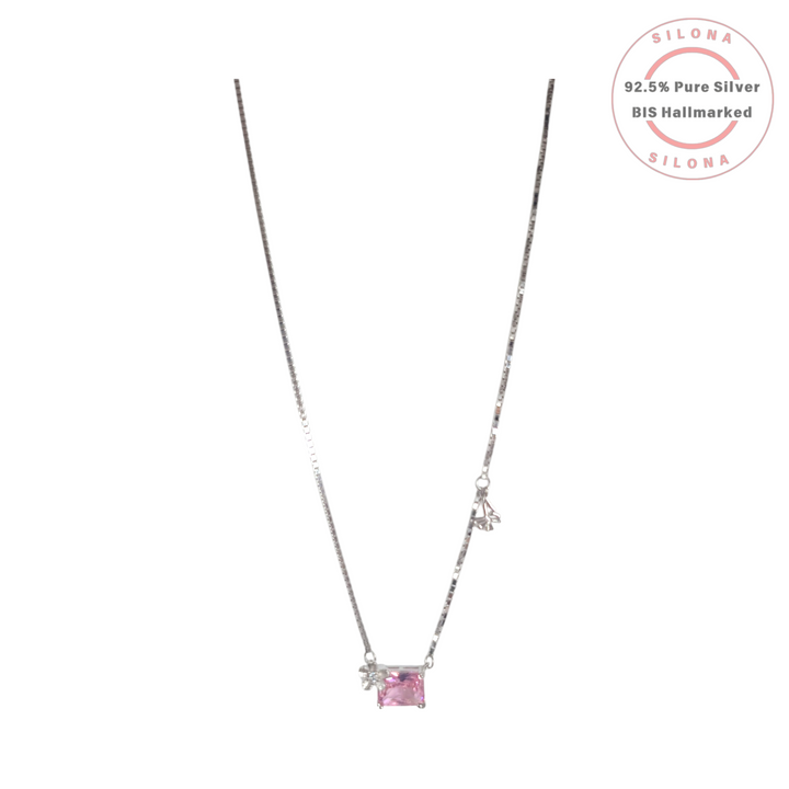 A delicate 92.5 silver box chain necklace featuring an off-center emerald-cut pink stone with a small silver bow accent.