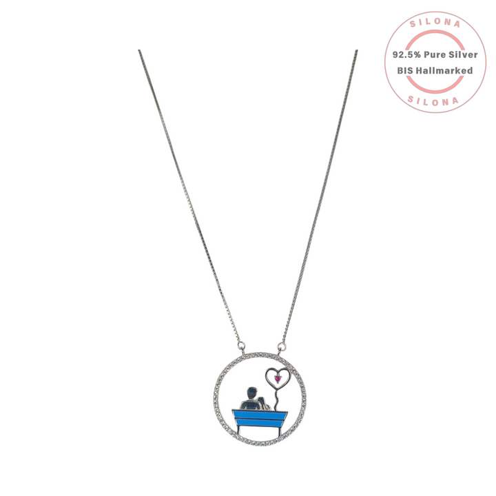 Silona's Enameled Couple Love Bench Necklace in 92.5 silver, featuring a couple on a blue bench with a pink heart balloon, on a white background.