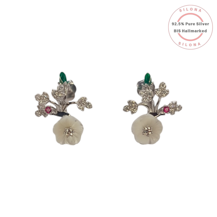 A pair of silver floral stud earrings with carved mother-of-pearl flowers, sparkling cubic zirconia leaves, and small red and green gemstone accents, on a white background.