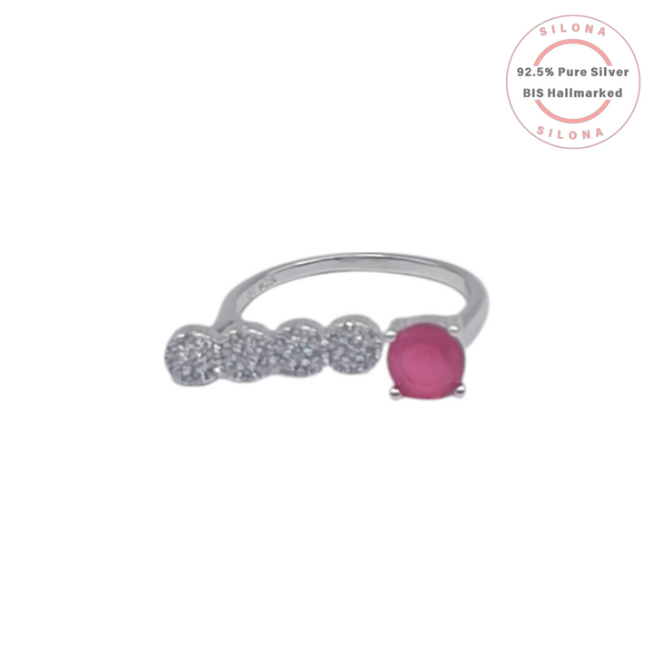 A modern open bypass ring in 92.5 silver, featuring a round ruby-hued stone on one end and a row of four clear pavé zircons on the other, on a white background.
