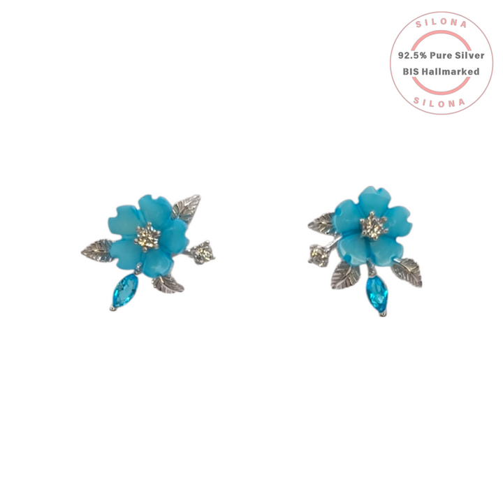 A pair of Silona floral stud earrings in 92.5 silver, featuring a turquoise blue flower with a crystal center and a matching marquise-cut crystal drop.