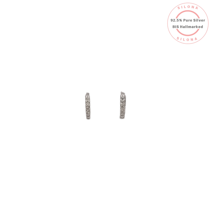 A pair of minimalist pavé cubic zirconia huggie earrings in 92.5 sterling silver on a white background.