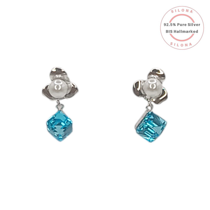 A pair of Silona silver drop earrings with a floral pearl stud and a dangling square-cut aquamarine blue crystal, on a white background.