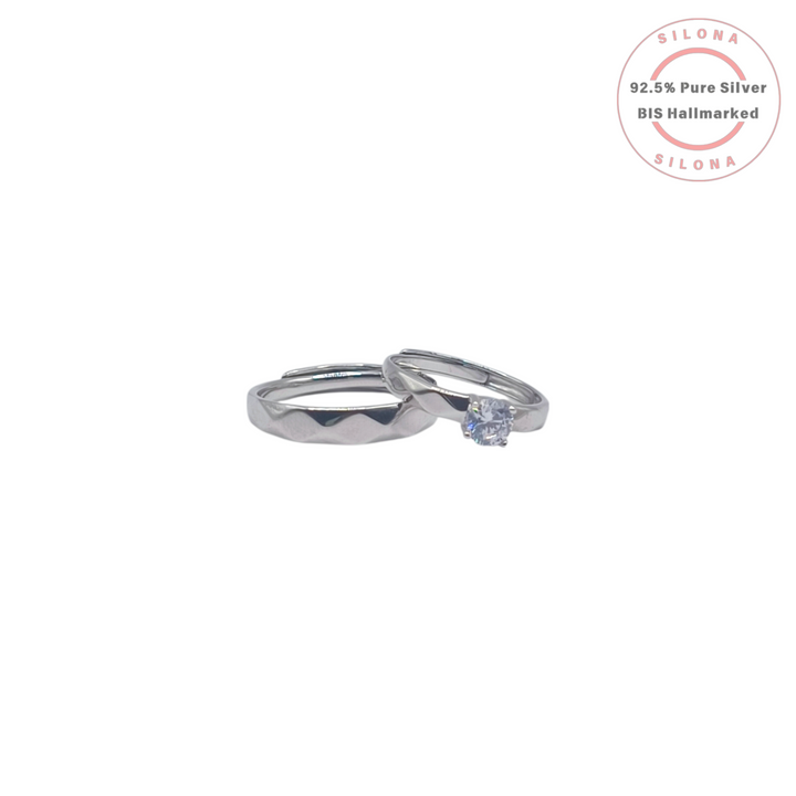 A pair of matching silver couple's rings, one with a solitaire cubic zirconia and one with a geometric band, on a white background.