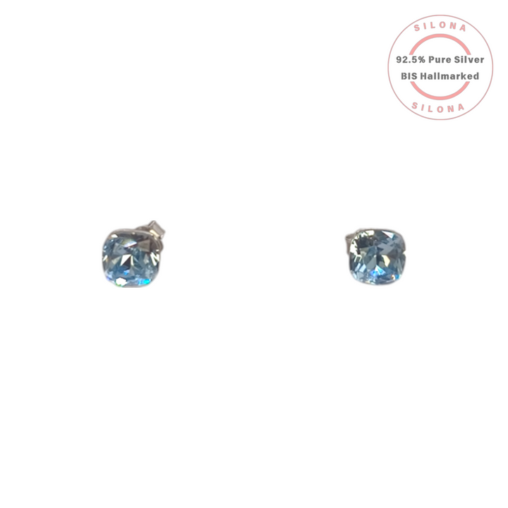 A pair of minimalist cushion-cut solitaire stud earrings with a light blue, aquamarine-colored stone, set in 92.5 sterling silver, on a white background.
