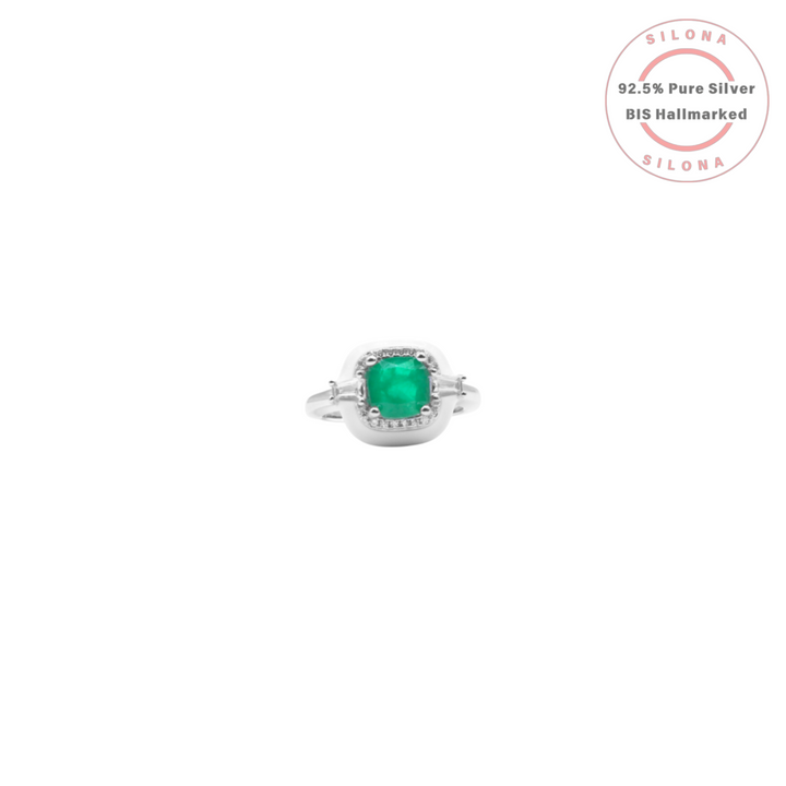 Front view of a silver ring featuring a cushion-cut emerald-green cubic zirconia surrounded by a halo of smaller stones and flanked by baguette-cut stones, on a white background.