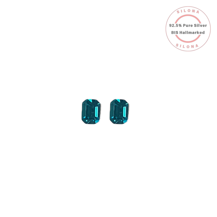 A pair of Silona emerald-cut stud earrings featuring deep peacock blue stones, crafted in 92.5 sterling silver, shown on a white background.