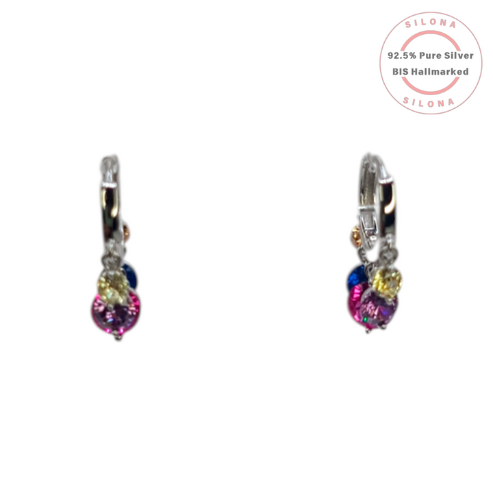 A pair of Silona silver huggie hoop earrings with a dangling cluster of colorful pink, blue, and yellow cubic zirconia stones on a white background.