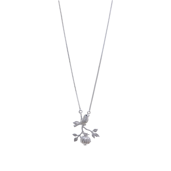 A silver box chain holding a pendant of a detailed bird perched on a branch with leaves and hanging fruit.